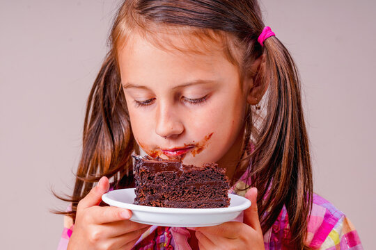 Funny portrait of very happy stained young girl eating a chocolate cake.