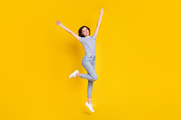 Fototapeta na wymiar Full length photo of shiny young woman raise hands jumping high good mood dressed trendy striped look isolated on yellow color background