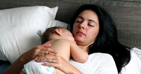 Mother and baby sleeping together in bedroom. Mom lying in bed with infant child asleep