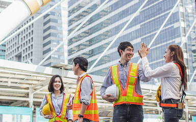 Group of four engineering inspectors wearing hard hat, uniform for safety, high five, teamwork working with success, finish or complete construction, confidently smiling, standing outdoor site.