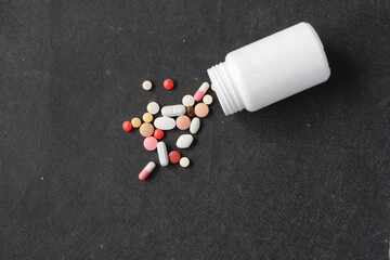 many colorful pills and capsules spilling form a white container on black 