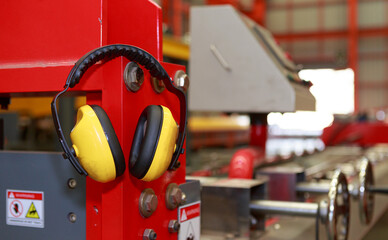 Yellow protective earmuffs hang on heavy industrial machines. This concept is a PPE device.