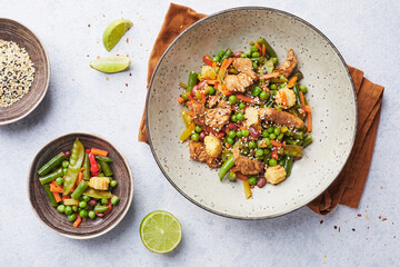 Wok with turkey meat, corn, green peas, green beans and carrots served on gray background with chopsticks. Asian food concept of street food