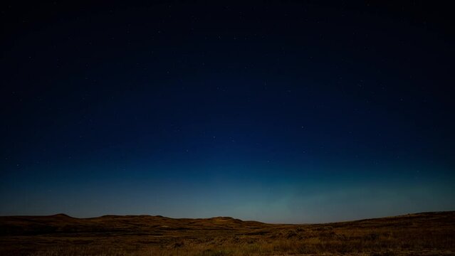 Dark blue night sky with moving stars and Aurora flashing on the horizon. Set the prairies in autumn.  