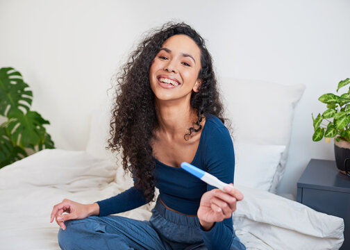 A young happy multi-ethnic woman holds pregnancy test smiling at camera