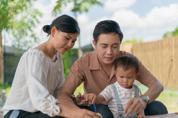 Asian family with baby little son painting eggs with brush in class workshop. Happy Asian father and mother with little son and teaching painting eggs with water colour