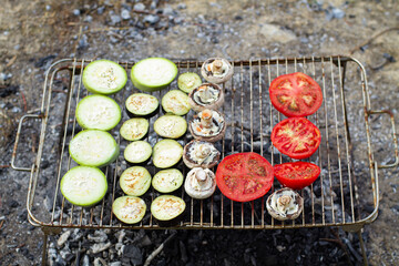 Hot organic healthy vegetables:sliced tomato, zucchini, champignon and eggplant being grilled on outdoor barbeque grill.Summer picnic and vegetarian food.Outdoor recreation.Food cooked over a campfire