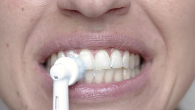 woman using electric tooth brush for teeth daily cleaning routine.smiling girl with yellow tone teeth from coffee smoke red wine bad habits.natural not perfect straight,little bit crooked teeth.4k