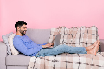Fototapeta premium Photo of cute sweet arab guy dressed blue pullover lying couch typing modern device isolated pink color background