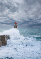 Fécamp's red lighthouse hit by a crashing wave on a storm day - sea lighthouse with dramatic sky,...
