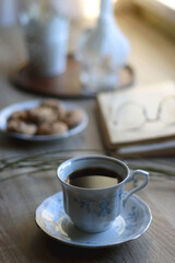 Cup of tea, plate with chocolate chip cookies, open book, reading glasses, lit candles and dry lavender flowers. Hygge at home, selective focus.