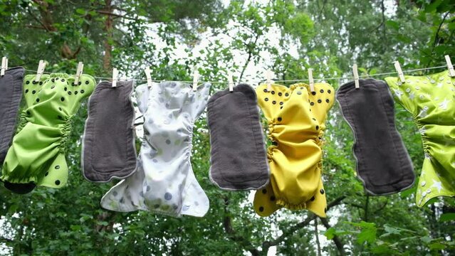 Reusable diapers are dried on clothesline outside in garden. Modern eco friendly cloth nappy for infant child hygiene. Sustainable lifestyle, zero waste concept.