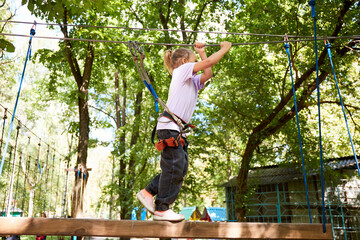 Portrait of brave little girl walk on a rope bridge in an adventure rope park. Having fun at adventure park. Scout practicing rappelling