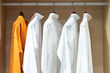 Shirts hang in a walking closet with glass door. One of those is in orange standout from others that are in white.