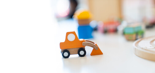 An orange wooden toy excavator is placed on the table in front of other blurry wooden toys.