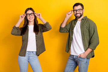 Portrait of attractive cheerful smart clever couple touching specs posing isolated over bright yellow color background