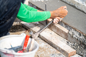 Labour in green long sleeve shirt using both hands to lever a wood with steel hammer inside a construction site.