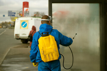 Fototapeta premium Guy washes bus stop. Worker with canister of water. Spraying detergent on glass.