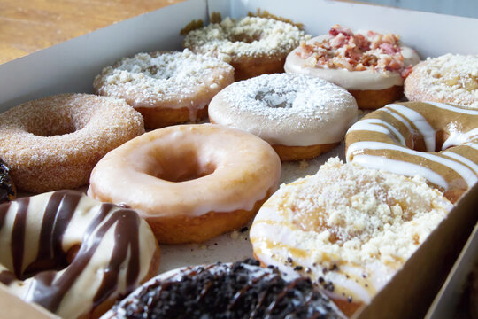 Picture of assorted donuts in a box with chocolate frosted, glazed and Bacon donuts.