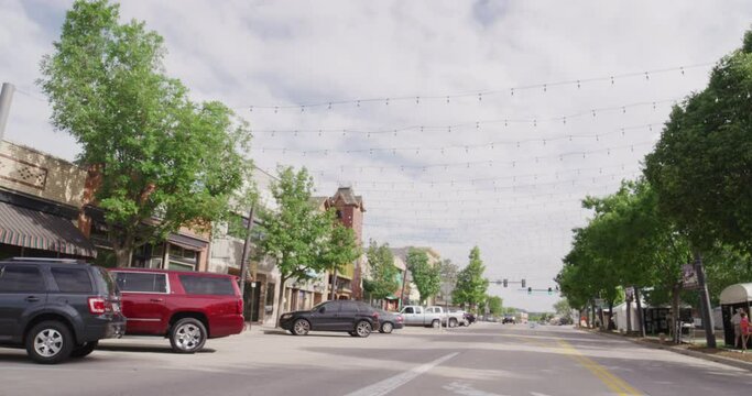 Panning on downtown main street in Castle Rock, Colorado on sunny summer day under strings on twinkle lights in slow motion