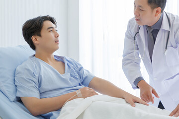 Senior doctor and young male patient who lie on the bed while checking symptom, consult and explain  in hospital wards.
