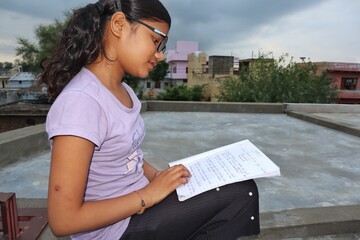 A eleven years old girl reading book, studing at the roof , indian little girl studing, self...