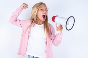caucasian blonde little girl wearing pink jacket and glasses over white background communicates shouting loud holding a megaphone, expressing success and positive concept, idea for marketing or sales.