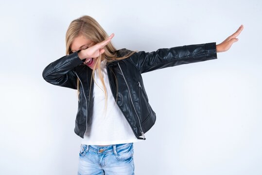 Photo of funky beautiful caucasian blonde little girl wearing biker jacket and glasses over white background show disco move dab