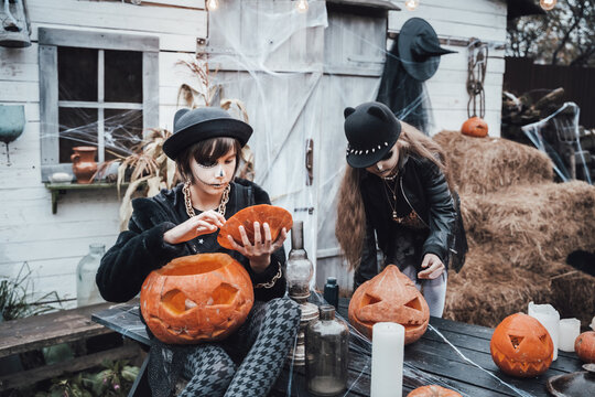 Beautiful scary little girls celebrating halloween. Terrifying black, white half-face makeup,witch costume, stylish image.Fun at children's party in barn on street. Hat, jacket,pumpkin jack-o-lantern