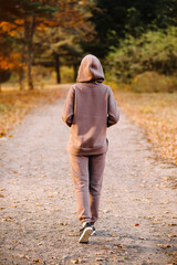 Young woman in hooded sweatshirt walking in an autumn park. Back view. Sunny weather. Fall season.