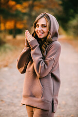 Young woman in hooded sweatshirt smiling in an autumn park. Sunny weather. Fall season.