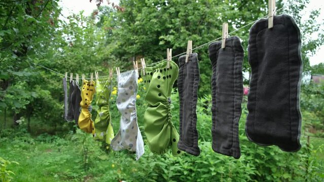 Reusable diapers are dried on clothesline outside in garden. Modern eco friendly cloth nappy for infant child hygiene. Sustainable lifestyle, zero waste concept.