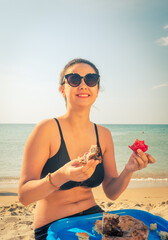 Hungry teenager brunette girl eating meat and tomato on the seaside.Picnic on the beach