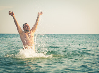 content mature man in swimming trunks playing with splattering aqua in wavy ocean on sunny day