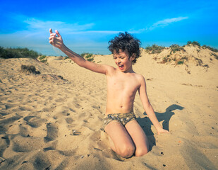 Cute little brunet boy on the beach plays with sand. kids travel concept. Sea holidays, copy space.