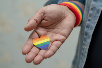 Asian lady wearing blue jean jacket or denim shirt and holding rainbow color flag heart, symbol of LGBT pride month celebrate annual in June social of gay, lesbian, bisexual, transgender.
