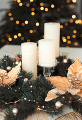 Christmas composition festive fir wreath with candles and decorations in gold color on the table against the background of a Christmas tree with warm lights