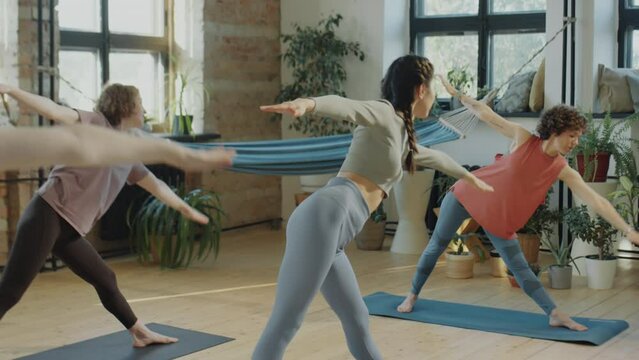 Group of girls doing extended triangle pose while having practice in yoga studio