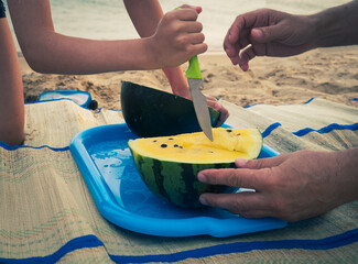 Hands of a child and father with a watermelon and a knife on the beach. Healthy food concept