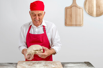 Chef-cooker in chef's hat and apron working in bakery, kneading dough for bread. Senior...