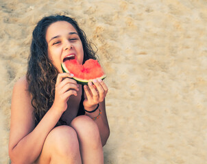 Smiling beautiful girl with dark long hair on the beach eating watermelon