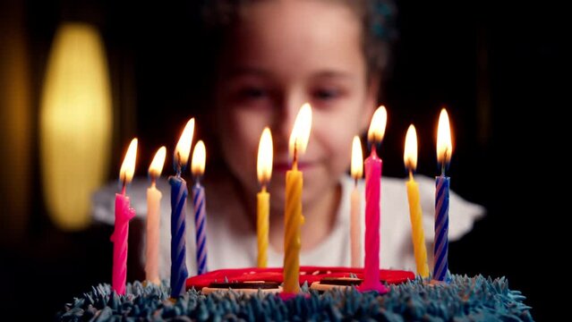 Portrait child celebrating birthday indoors at home. Little girl sitting at the table, child on her birthday makes wish before blowing out the candles on birthday cake.