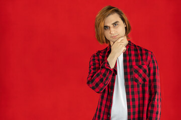 Young man Prep Student with long hair. Portrait of a guy with hand on chin. Red background