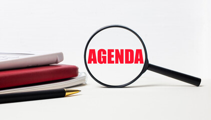 Office table with notepads, black calculator, pen and magnifying glass with AGENDA inscription. Side view.