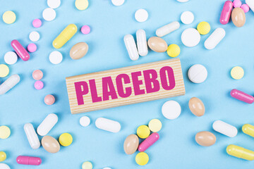 On a blue background, multi-colored pills and a wooden block with the text PLACEBO. View from above. Medical concept