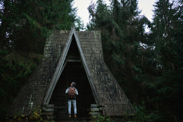 Men traveler standing inside old wooden dark house among woodland. Gloomy dark vintage style image