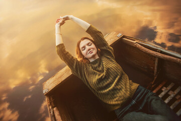 A beautiful blonde woman in a vintage sweater, with her eyes closed, lies in an old rowing boat...