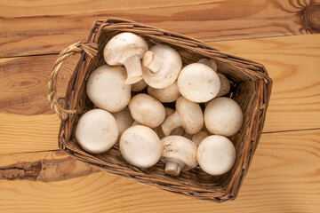 Several fresh organic mushrooms in a basket on a wooden table, close-up, top view.