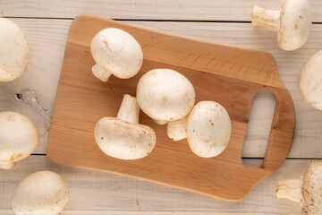 Several fresh organic mushrooms with a wooden dividing board on a wooden table, close-up, top view.