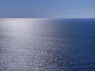 Fototapeta na wymiar Shiny sliver sea and blue sky. Glittering seascape with calm water surface.